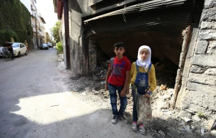 12-year-old twins stand near garbage outside a building in the old city of Homs, Syria.   UNICEF.