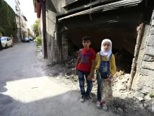12-year-old twins from the old city of Homs stand near garbage outside a dilapidated building. 