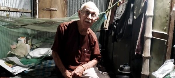 The simple living quarters of Father Robert Terence McCahill in a school building in Srinagar, Munshigonj district, Bangladesh, shown on Nov. 18, 2025. The 5-by-8-foot space provided free by local authorities contains a wooden bed, mosquito net, kerosene stove, and bicycle. Credit: Stephan Uttom Rozario