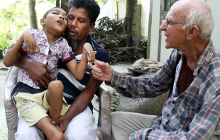Abdul Mannan Khan and his disabled son Abu Mosa Khan meet with Father Robert Terence McCahill at their home in Munshigonj district, Bangladesh, on Nov. 18, 2025. The priest visits villages daily to find disabled children and connect them with medical treatment. Credit: Stephan Uttom Rozario