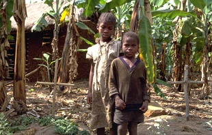 AIDS orphans Dominic, 7, and her sister Reticia, 10, standing between parents' graves in this December 2000 file photo.   UN Photo/Louise Gubb.