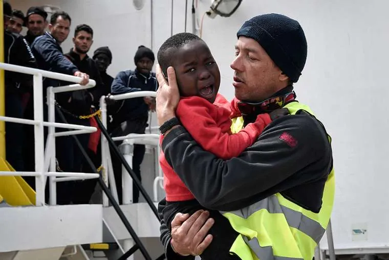A helper from Doctors Without Borders holds a Nigerian child as a migrant ship arrives at a Sicilian port May 14, 2018. ?w=200&h=150