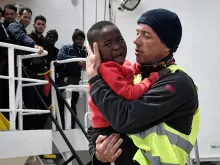 A helper from Doctors Without Borders holds a Nigerian child as the MV Aquarius arrives at the Sicilian port of Messina, on May 14, 2018. 