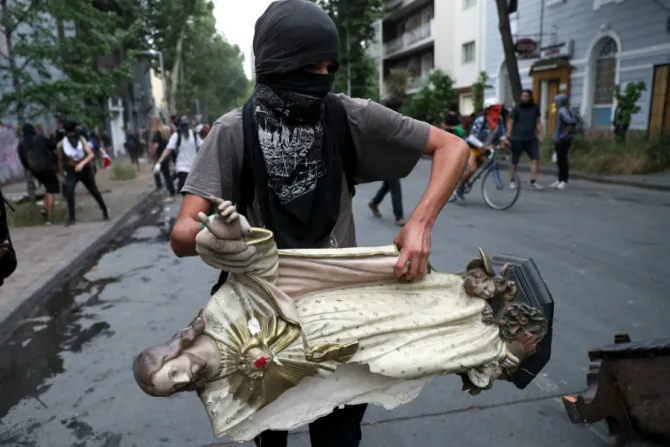A masked demonstrator carries a statue of Christ that he took from a church to be added to a barricade in Santiago Chile Credit Esteban Felix AP Shutterstock