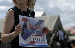 A woman holds a sign encouraging people to vote. ?w=200&h=150