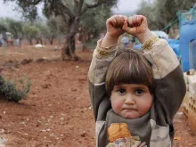 A young Syrian child raises her arms in a gesture of surrender. 