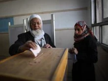 An election official (R) watches as an elderly man votes at a polling station in Old Cairo. 