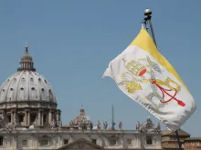 The flag of Vatican City with St. Peter’s Basilica in the background. 