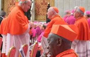Cardinal Bernard Agre of Abidjan, Ivory Coast reads his program while Cardinal Christoph Schonborn greets a friend 