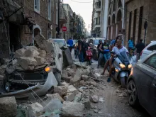 People ride past a car destroyed after a building wall collapsed after a large explosion on August 4, 2020 in Beirut, Lebanon. 