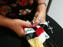 Christina Shabo holds a rosary and a scarf of the Iraqi flag. 