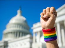 Hand wearing gay pride rainbow wristband making a power fist gesture in front of the US Capitol building in Washington, DC  Credit: lazyllama/Shutterstock