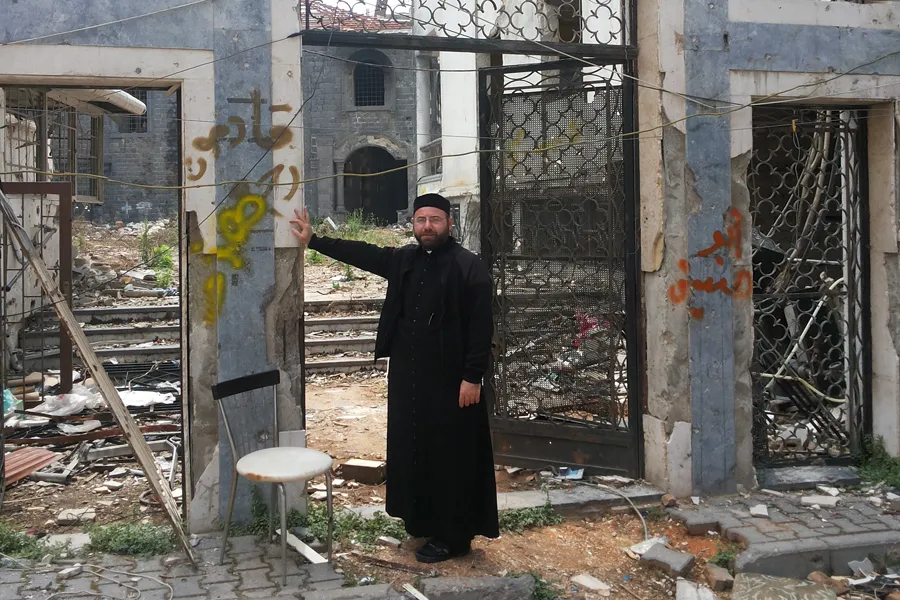 A priest stands before the ruins of St. Mary's Syriac Orthodox parish in Homs. ?w=200&h=150