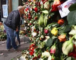 People look through a gate of flowers where behind it work continues at the scene of the bomb explosion in Oslo, Norway. ?w=200&h=150