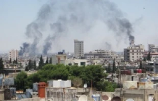Smoke billows skyward as homes and buildings are shelled June 9, 2012 in the city of Homs, Syria.   UN Photo-David Manyua.