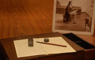 St. Therese of Lisieux's writing desk sits on display in front of a drawn image of the saint holding it in her lap.   Addie Mena/CNA.