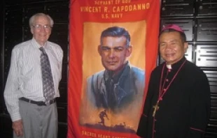 Ted Bronson and Bishop Joseph Tri stand in front of a banner of Servant of God Fr. Vincent Capodanno in Vietnam, June 2013.   Joan Lewis/EWTN.