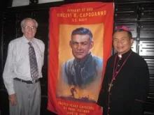 Ted Bronson and Bishop Joseph Tri stand in front of a banner of Servant of God Fr. Vincent Capodanno in Vietnam, June 2013. 
