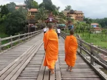 Young buddhist monks cross a bridge in Thailand. 