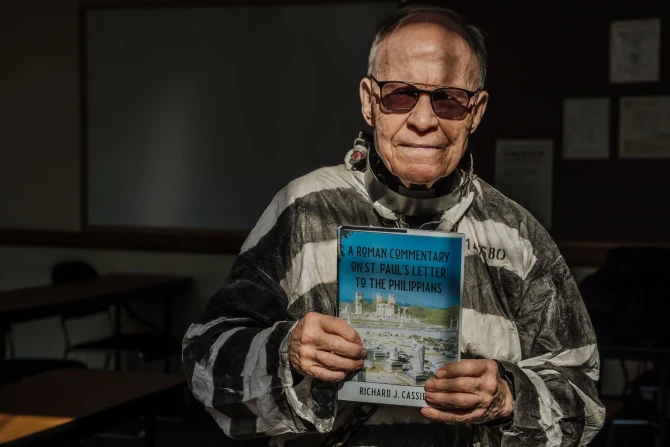 Fr. Richard Cassidy, professor of Sacred Scripture at Sacred Heart Major Seminary, dresses in Roman prisoner garb as he holds a copy of his newest book, "A Roman Commentary on St. Paul’s Letter to the Philippians."