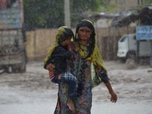 A woman carrying a child walks along a street during a heavy rainfall in the flood-hit Dera Allah Yar town in Jaffarabad district, Balochistan province, Pakistan, on Aug. 30, 2022. Aid efforts ramped up across flooded Pakistan to help tens of millions of people affected by relentless monsoon rains that have submerged a third of the country and claimed more than 1,100 lives.