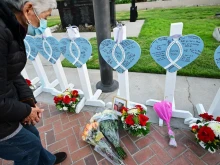A woman takes a closer look at the names of 11 people killed in a mass shooting written on crosses and displayed during a candlelight vigil in front of the City Hall in Monterey Park, California, on Jan. 24, 2023.