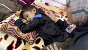 Eight-year-old Yamen Abu Hilal lies on a bed as a woman sits beside him in a hospital room in Gaza City, Gaza Strip, on Nov. 24, 2025.  His condition has sharply worsened amid the collapse of Gaza’s health care system, which has been unable to provide diagnostic tools, medication, or equipment since no medical supplies have entered the Strip following the ceasefire.