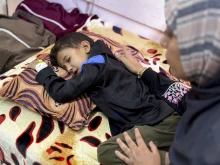 Eight-year-old Yamen Abu Hilal lies on a bed as a woman sits beside him in a hospital room in Gaza City, Gaza Strip, on Nov. 24, 2025.  His condition has sharply worsened amid the collapse of Gaza’s health care system, which has been unable to provide diagnostic tools, medication, or equipment since no medical supplies have entered the Strip following the ceasefire.