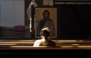 A woman sits alone in a Catholic church. Josh Applegate via Unsplash.com.