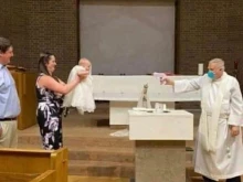 Fr. Stephen Klasek pretends to shoot water at a baby in this now-viral photo. 