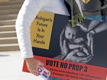 A woman carries a sign warning of the dangers of Proposal 3, the so-called "Reproductive Freedom for All" constitutional amendment, during an Oct. 15 rally at the state capitol building in Lansing. If the controversial proposal passes, it would mean the end of all abortion-related regulation in Michigan, including for children and minors.