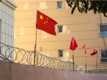 Chinese flags on barbed wired wall in Kashgar (Kashi), Xinjiang, China. Credit: Jonathan Densford/Shutterstock