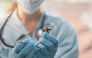 Doctor holding cross and praying.   Florin Deperin/Shutterstock