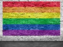 Rainbow flag painted over old white brick wall. Stock image via Shutterstock.