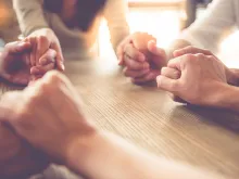 Women holding hands in prayer. Stock image via Shutterstock.