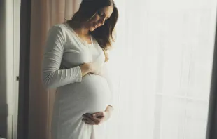 Pregnant woman standing by the window.   Shutterstock