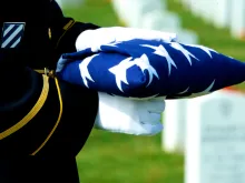 Honor Guard holding folded American flag at grave site at Arlington National Cemetery. Stock photo via Shutterstock