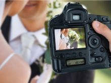 Photographer holding camera against couple at wedding. Via Shutterstock
