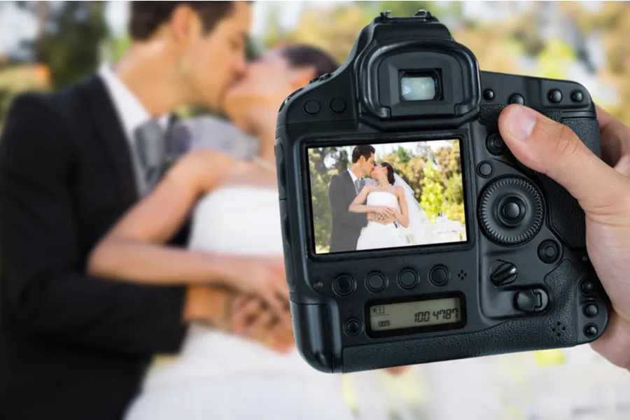 Photographer holding camera against newlywed couple. ?w=200&h=150
