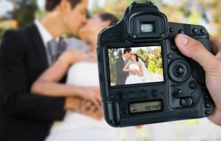 Photographer holding camera against newlywed couple. Credit: Vectorfusionart/Shutterstock