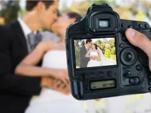 Photographer holding camera against newlywed couple. 