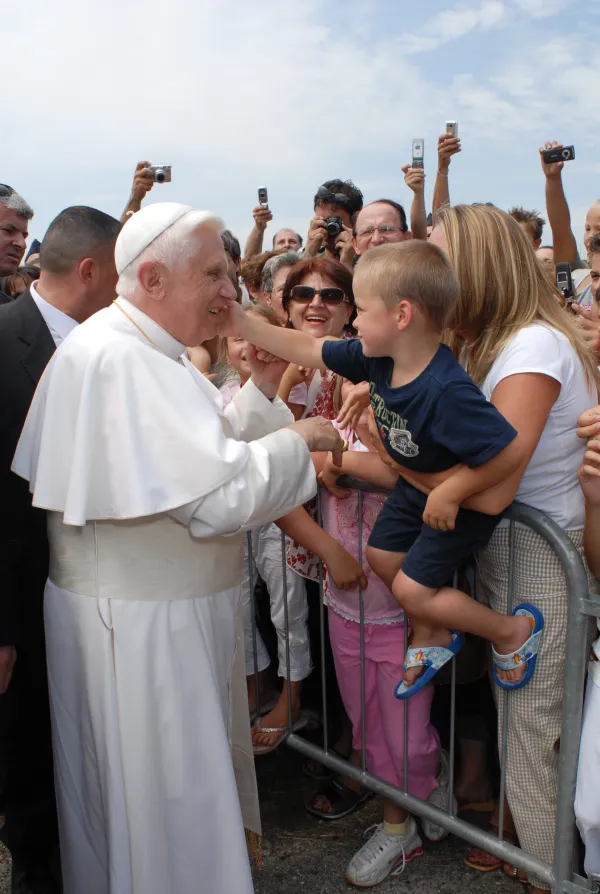 A child touches Pope Benedict XVI on the cheek as he greets pilgrims. Vatican Media.