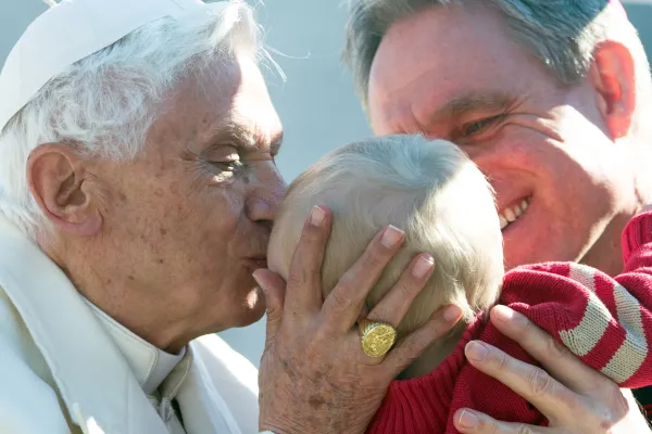 Pope Benedict XVI kisses a baby held by his head private secretary Archbishop Georg Ganswein. Ganswein remained Benedict's personal secretary throughout his pontificate and retirement. Vatican Media