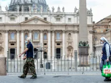 People wearing face coverings walk past St. Peter’s Basilica.