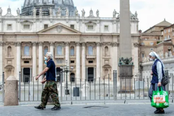 People wearing face coverings walk past St. Peter’s Basilica.