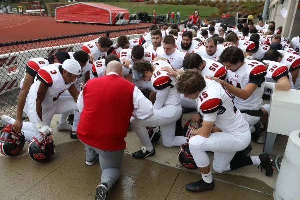 Mike "Gut" Gutelius (back to the camera), the head football coach at The Catholic University of America, leads his football team in prayer. The Catholic University of America
