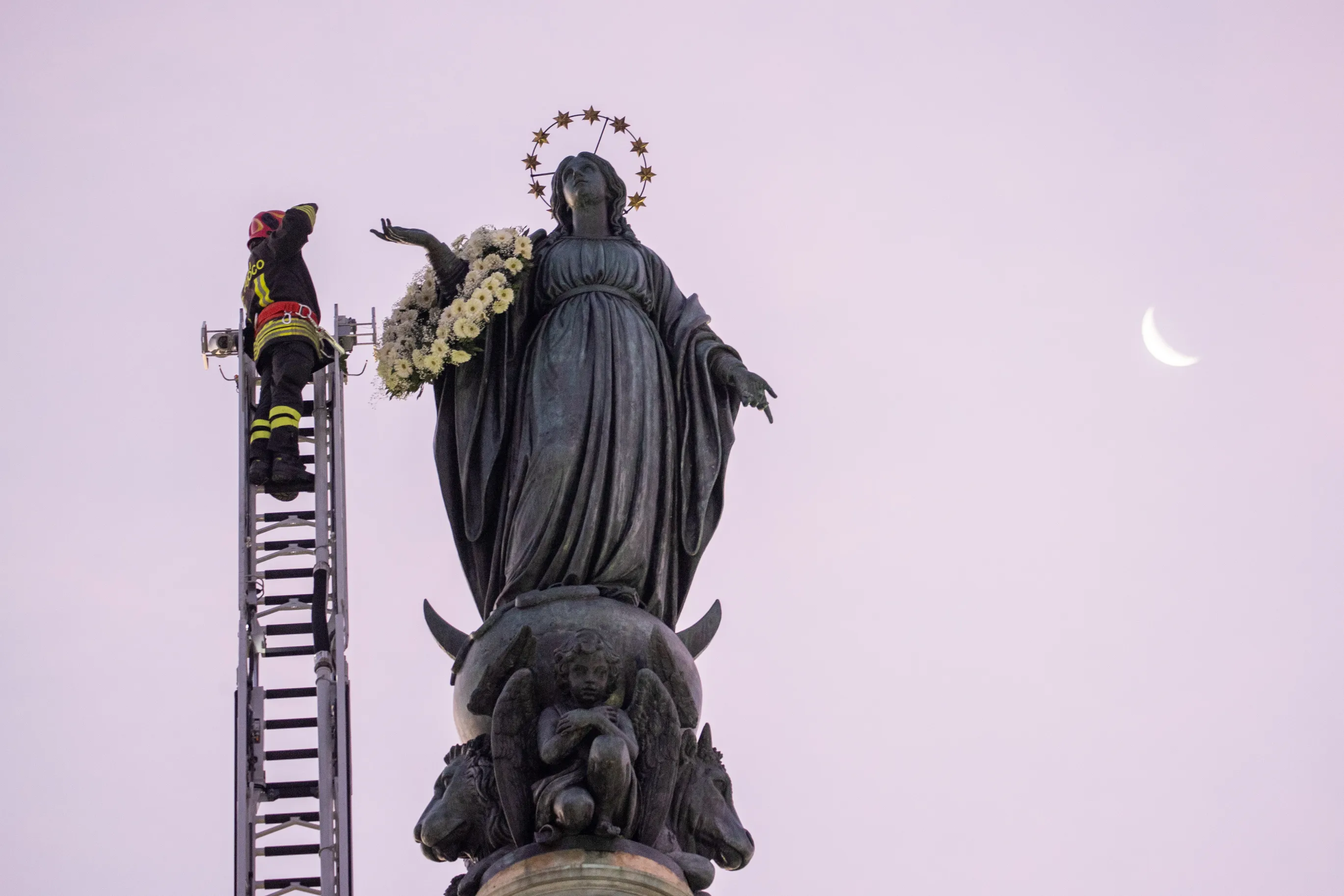A firefighter scales a long ladder to the top of a nearly 40-foot-high column to pay tribute at dawn to the Blessed Virgin with a wreath of flowers on Dec. 8, 2023.?w=200&h=150