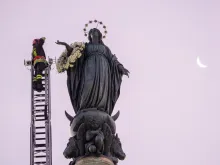 A firefighter scales a long ladder to the top of a nearly 40-foot-high column to pay tribute at dawn to the Blessed Virgin with a wreath of flowers on Dec. 8, 2023.