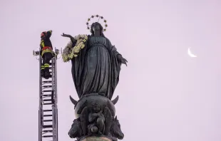 A firefighter scales a long ladder to the top of a nearly 40-foot-high column to pay tribute at dawn to the Blessed Virgin with a wreath of flowers on Dec. 8, 2023. Credit: Daniel Ibanez/CNA