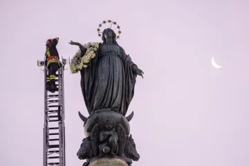 A firefighter in Rome pays tribute to the Blessed Virgin Mary by laying a wreath of fresh flowers at her statue atop a column near the Spanish Steps on Dec. 8, 2023.